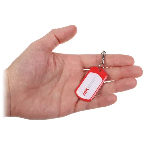 Osoba trzyma w dłoni czerwony brelok z logo Hikvision. Brelok ma prostokątny kształt z zaokrąglonymi rogami i jest przymocowany do metalowego łańcuszka.