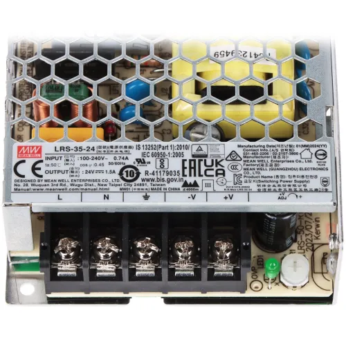 Zasilacz impulsowy z metalową obudową o strukturze plastra miodu, z widocznymi komponentami elektronicznymi i złączami. Na obudowie znajdują się oznaczenia techniczne i certyfikaty.