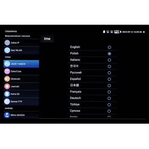 Menu ustawień urządzenia elektronicznego z wyświetlonymi opcjami językowymi, takimi jak angielski, polski i inne. Po lewej stronie widoczne są dodatkowe opcje ustawień, takie jak adres IP, sieć WLAN i data/czas.