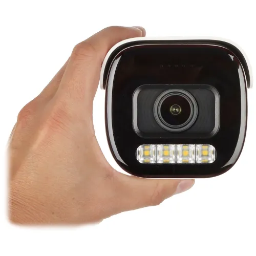 Na zdjęciu widać rękę trzymającą kamerę monitoringu z widocznym obiektywem i diodami LED. Kamera ma czarną obudowę z białymi elementami.