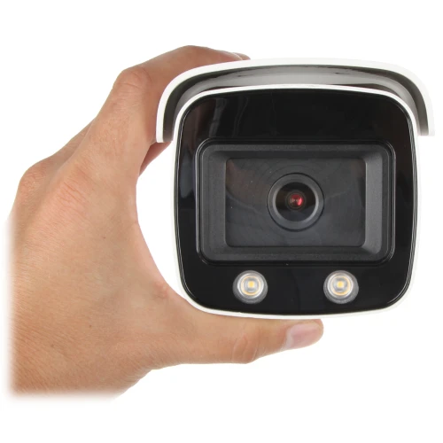 Kamera monitoringu w białej obudowie z czarnym panelem frontowym, wyposażona w dwa diody LED i centralnie umieszczony obiektyw. Produkt jest trzymany w dłoni, co ukazuje jego kompaktowy rozmiar.