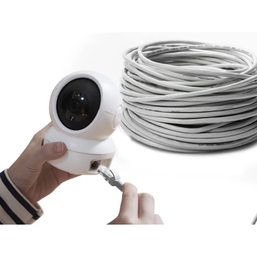 Osoba podłącza kabel sieciowy do białej kamery monitorującej o zaokrąglonym kształcie. W tle widoczna jest zwinięta wiązka białego kabla.