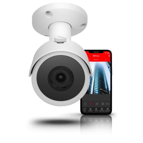 Biała kamera sieciowa IP zamontowana na suficie, z widocznym obiektywem skierowanym w dół. W tle znajduje się smartfon z aplikacją pokazującą obraz z kamery.