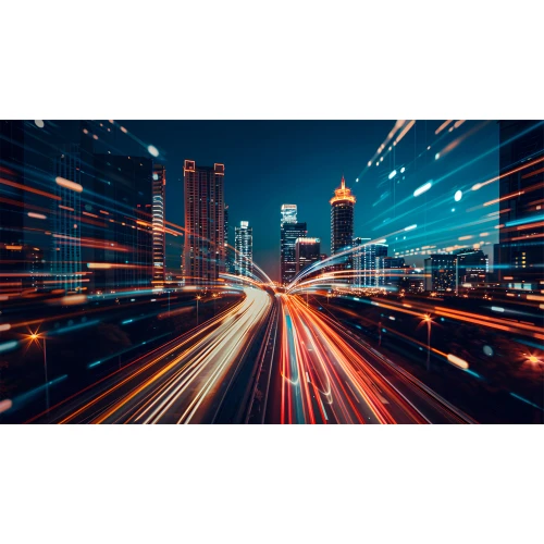 Zdjęcie przedstawia nowoczesne miasto nocą z dynamicznymi smugami świateł samochodów na autostradzie. W tle widać oświetlone wieżowce, tworzące futurystyczny krajobraz.