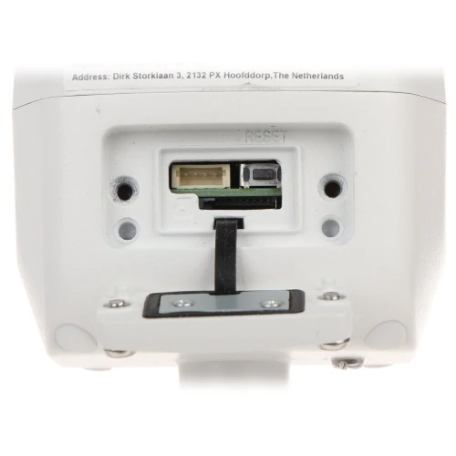 Zdjęcie przedstawia spód urządzenia elektronicznego z widocznymi portami i przyciskiem reset. Na obudowie znajduje się również etykieta z adresem producenta.