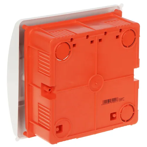 Czerwone, plastikowe pudełko montażowe z widocznymi otworami na przewody i mocowania. Pudełko jest umieszczone na białej podstawie, widocznej z boku.