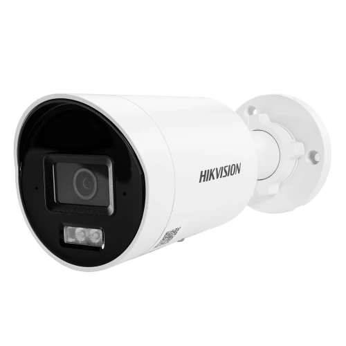 Biała kamera monitoringu marki Hikvision z czarnym panelem przednim i obiektywem znajduje się na tle. Kamera jest zamontowana na uchwycie ściennym, co umożliwia jej łatwe ustawienie.
